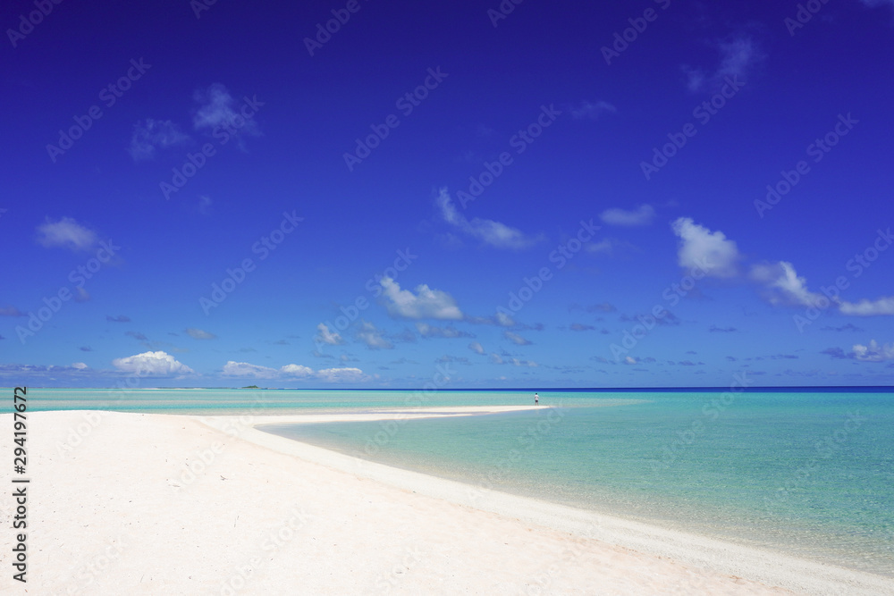 A man looks out over a tropical turquoise lagoon from a white sandy beach under a blue sky with copy space