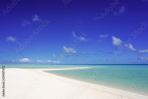 Fototapeta Naklejka Na Ścianę i Meble -  A man looks out over a tropical turquoise lagoon from a white sandy beach under a blue sky with copy space