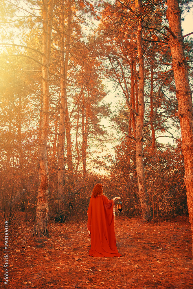 Woman in red holding a lantern with a candle. Hand lantern with a candle shines in the woods. Woman in red holding a lantern with a candle. Hand lantern with a candle shines in the woods.