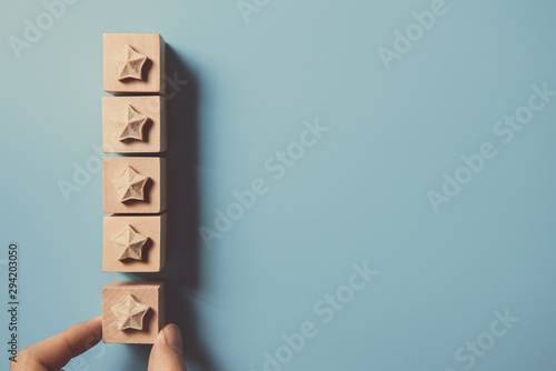 Fotografija Man Hand putting wooden five star shape on blue background