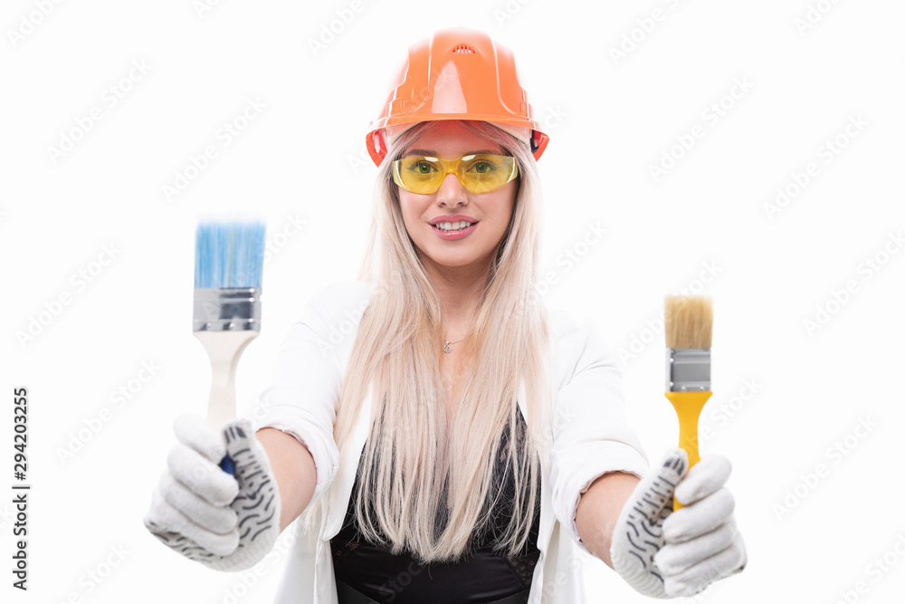 The blonde in the orange construction helmet and safety glasses holding in his hand the construction of the brush for painting The blonde in the orange construction helmet and safety glasses holding in his hand the construction of the brush for painting