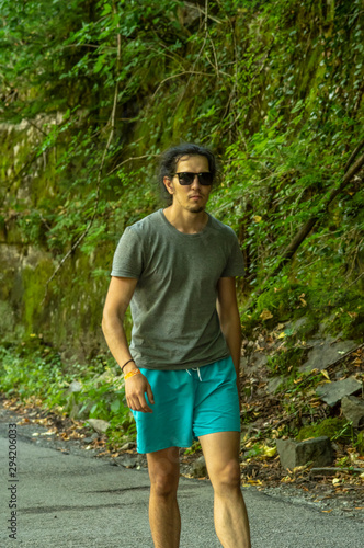 Walk in the fresh air. A young man with glasses looks at the nature around him. A man walks along the road.