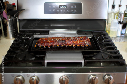 Marinated St. Louis cut pork ribs baked on a carbon steel tray, resting on the stove top in a home kitchen.