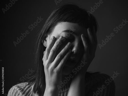 Sad young woman with hands on face. Black and white. Close up