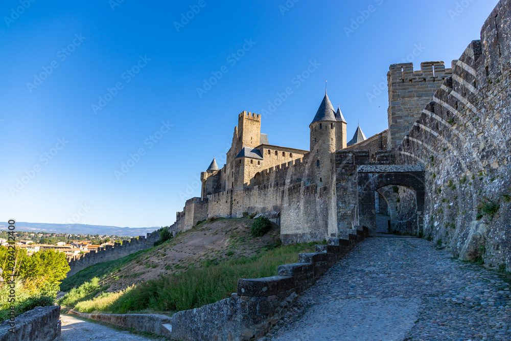Outer wall of the fortified city of Carcassonne. Beautiful medieval castle at morning in the background of blue sky. High walls with towers of famous Cité de Carcassonne. Occitanie region, France.