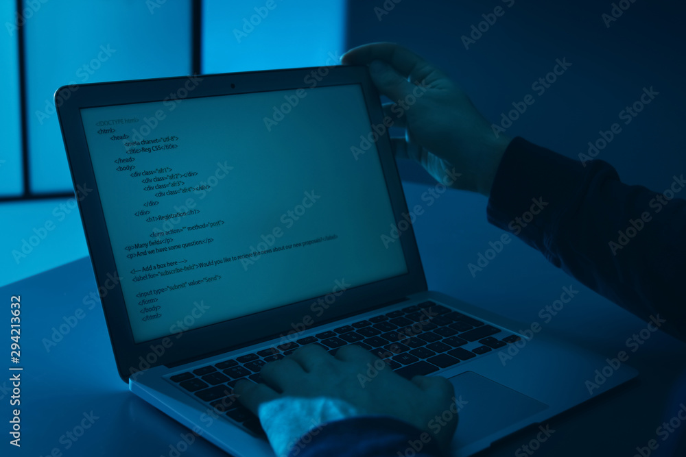 Man using laptop at table in dark room, closeup. Criminal offence Man using laptop at table in dark room, closeup. Criminal offence