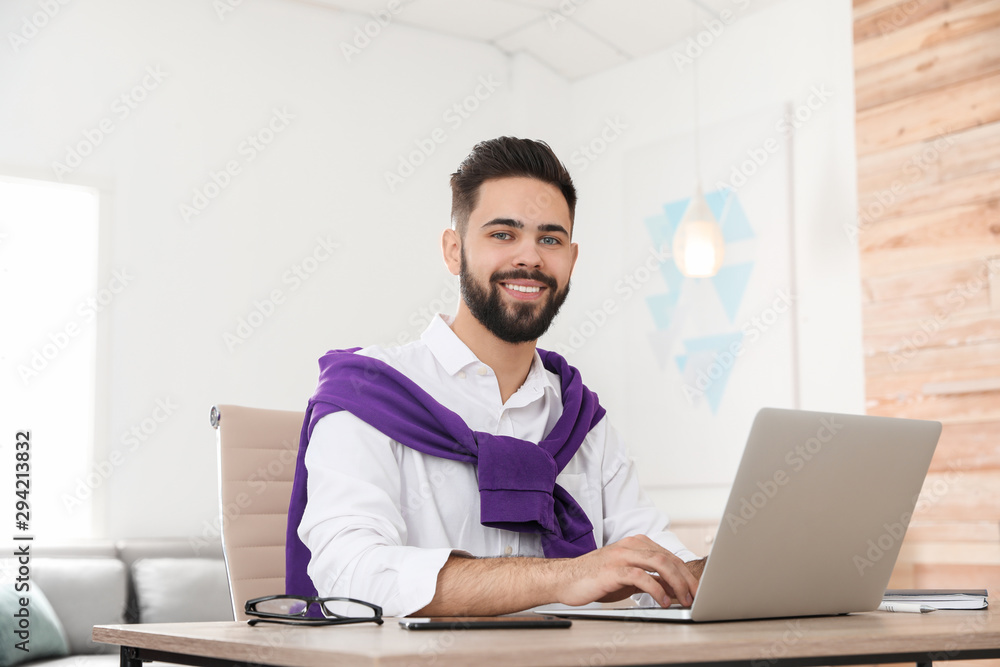 Handsome young man working with laptop at table in home office Handsome young man working with laptop at table in home office