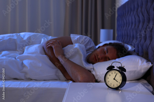 Konstfotografi Alarm clock on nightstand near sleeping young man. Bedtime