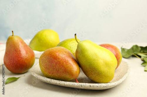 Plate with ripe juicy pears on stone table against light background