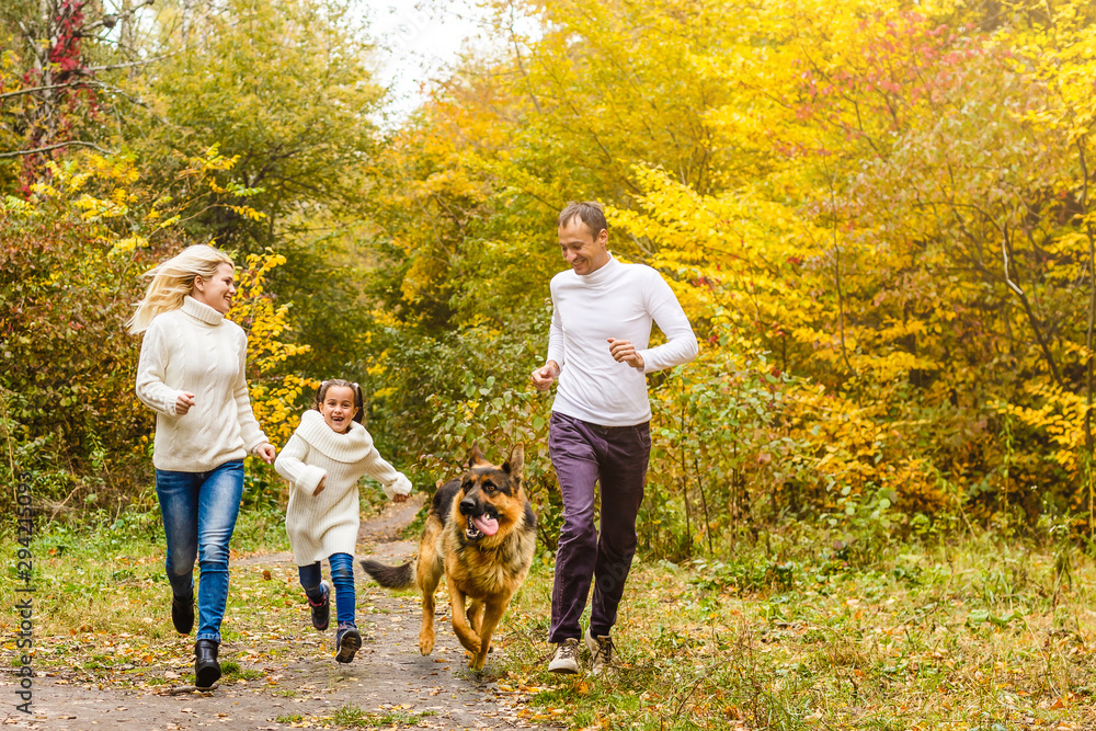 Happy family with children running after a dog together in autumn park - obrazy, fototapety, plakaty 