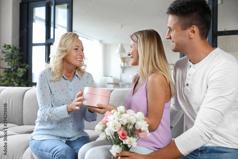 Young couple with bouquet and gift box congratulating their mother in living room Young couple with bouquet and gift box congratulating their mother in living room