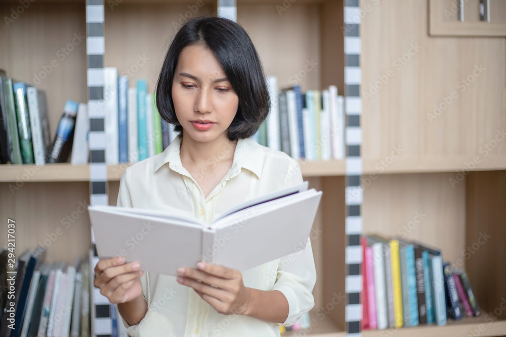 Young and beautiful businesswoman holding a book in her hands and reading at the bookshelves in the modern office Young and beautiful businesswoman holding a book in her hands and reading at the bookshelves in the modern office