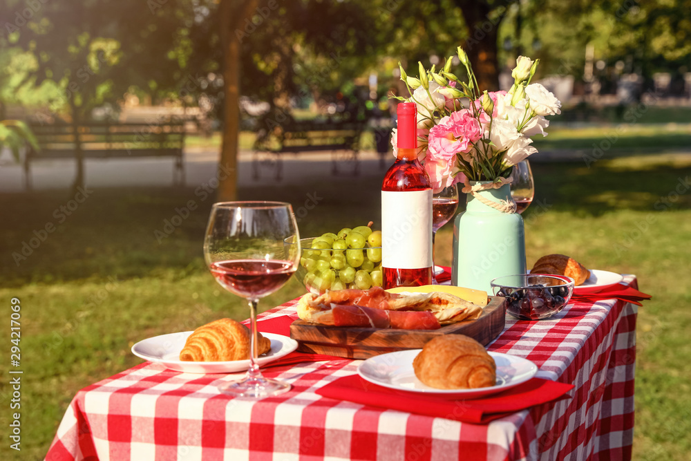 Wine, food and flowers on picnic table in park on sunny day
