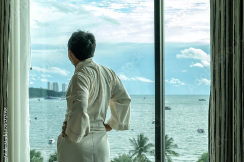 Behide asian man in bathrobe suit open curtain to see view outside in morning, Travel and Holiday concept © Pornchai