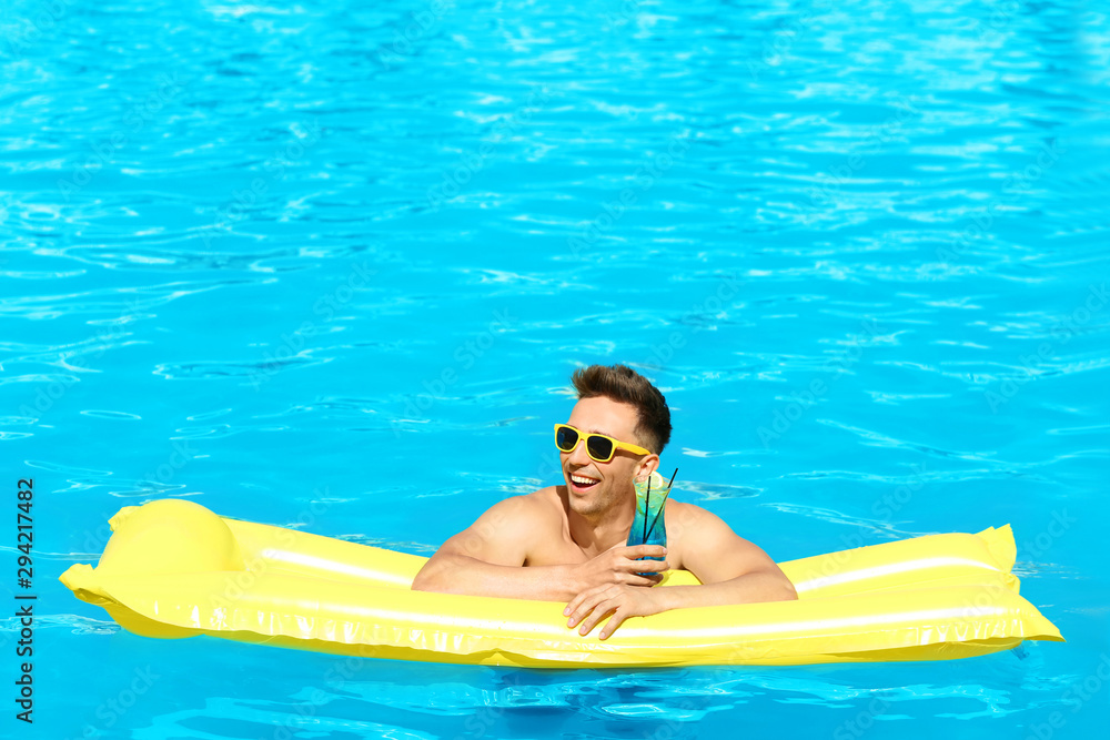 Happy young man with cocktail and inflatable mattress in swimming pool