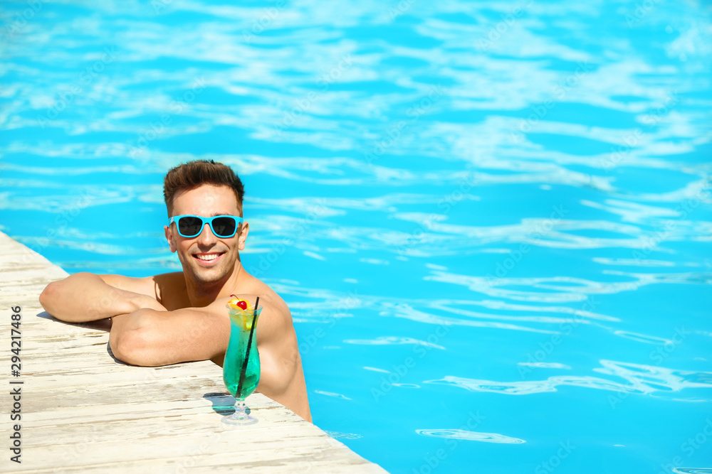 Happy young man with cocktail in swimming pool