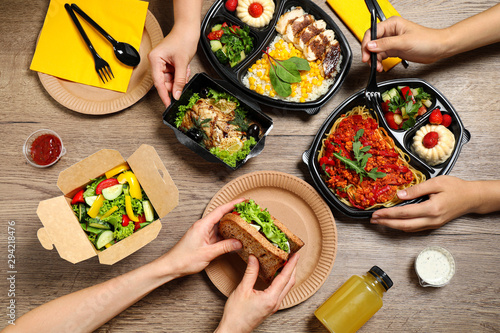 People eating healthy meals at wooden table, top view. Food delivery