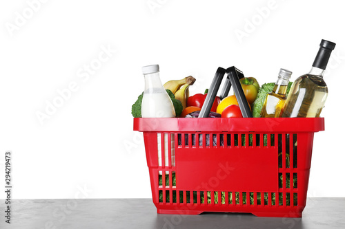 Shopping basket with grocery products on grey table against white background. Space for text