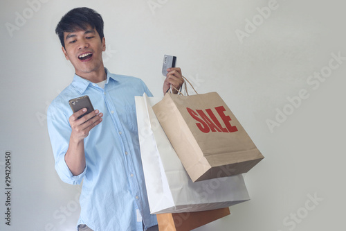 Asian  smilely man holding paper shopping bag and smart phone. photo