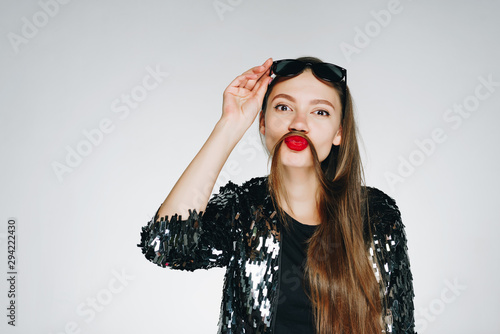 Glamorous young girl with dark long hair in a shiny black sweater and black t-shirt with sunglasses on her head on the white background fooling around and ready to go to a party