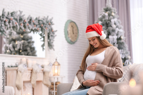 Young pregnant woman sitting on sofa in room decorated for Christmas