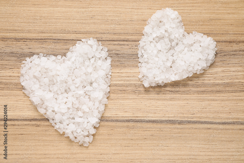 Heart shaped piles of sea salt for spa scrubbing procedure on wooden background, flat lay Heart shaped piles of sea salt for spa scrubbing procedure on wooden background, flat lay