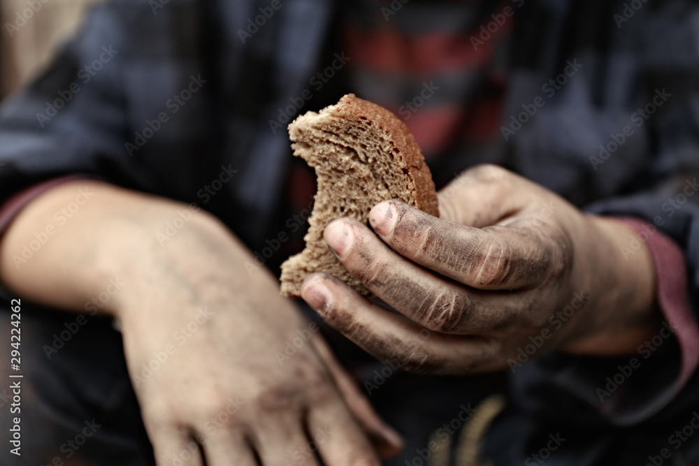 Poor homeless child with piece of bread outdoors, closeup