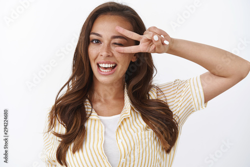 Close-up cheerful upbeat female express goodwill and positivity, feeling excellent after trying new product, smiling toothy satisfactory, wink playful, showing peace, victory sign, white background