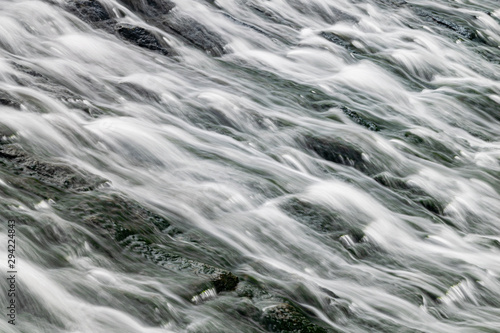 Long exposure of water flowing over algae covered rocks at Lopwell Weir, Plymouth, Devon photo