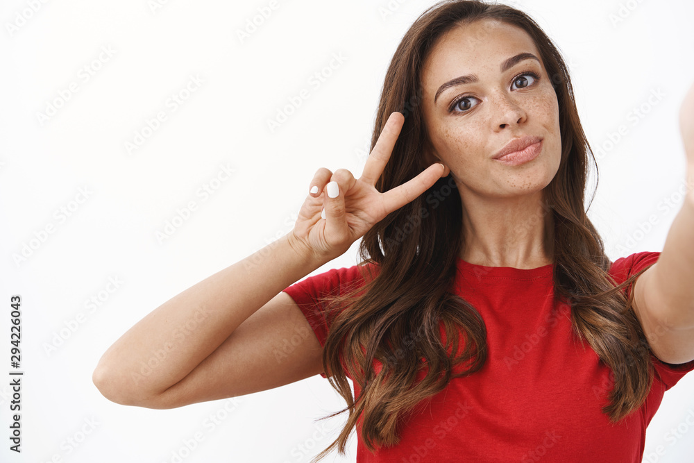 Close-up feminine athletic sensual young brunette with cute freckles, taking selfie in red t-shirt extend one hand hold camera, using smartphone make photograph, show peace or victory sign