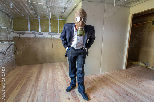 Strange man in businessman suit and gas protection mask inside a room under renovation works.