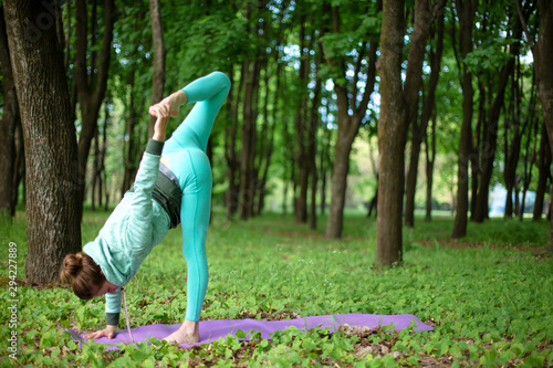 Fototapeta Naklejka Na Ścianę i Meble -  A young sports girl practices yoga in a quit green summer forest, yoga assans posture. Meditation and unity with nature