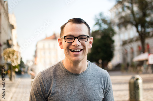 Half body shot of young man in a street of an old town in Europe looking in the camera with brown eyes and eyesglasses