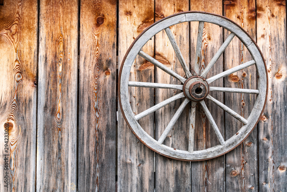 A wooden wheel with a metal hoop hangs on a wall made of old wooden planks. A wooden wheel with a metal hoop hangs on a wall made of old wooden planks.