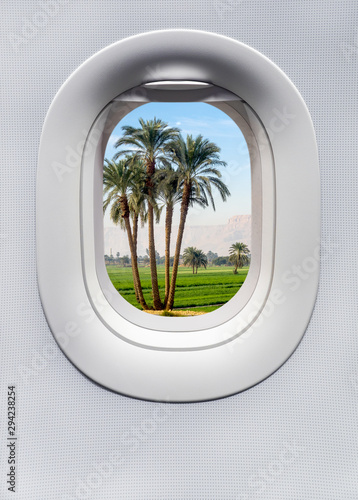Fotografie Travel landscape with green palm trees, view through airplane porthole window
