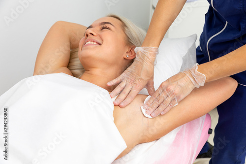 beautician lubricates wax under the arms of the client. hair removal with wax