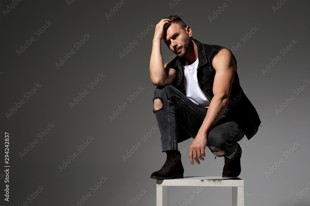 Thoughtful man adjusting his hair while squatting on a chair Thoughtful man adjusting his hair while squatting on a chair