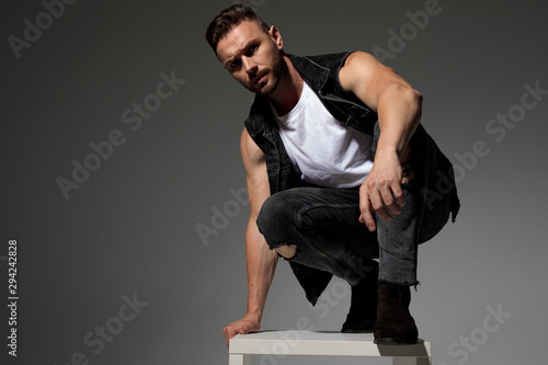 Tough casual man squatting and leaning on a chair