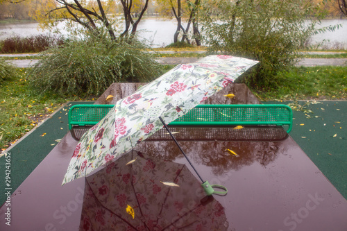 A light umbrella on a wet ping-pong table with a reflection in the rain on a cloudy autumn day photo