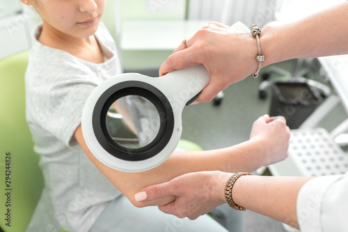 A dermatologist examines a teenagers skin condition with a dermatoscope photo