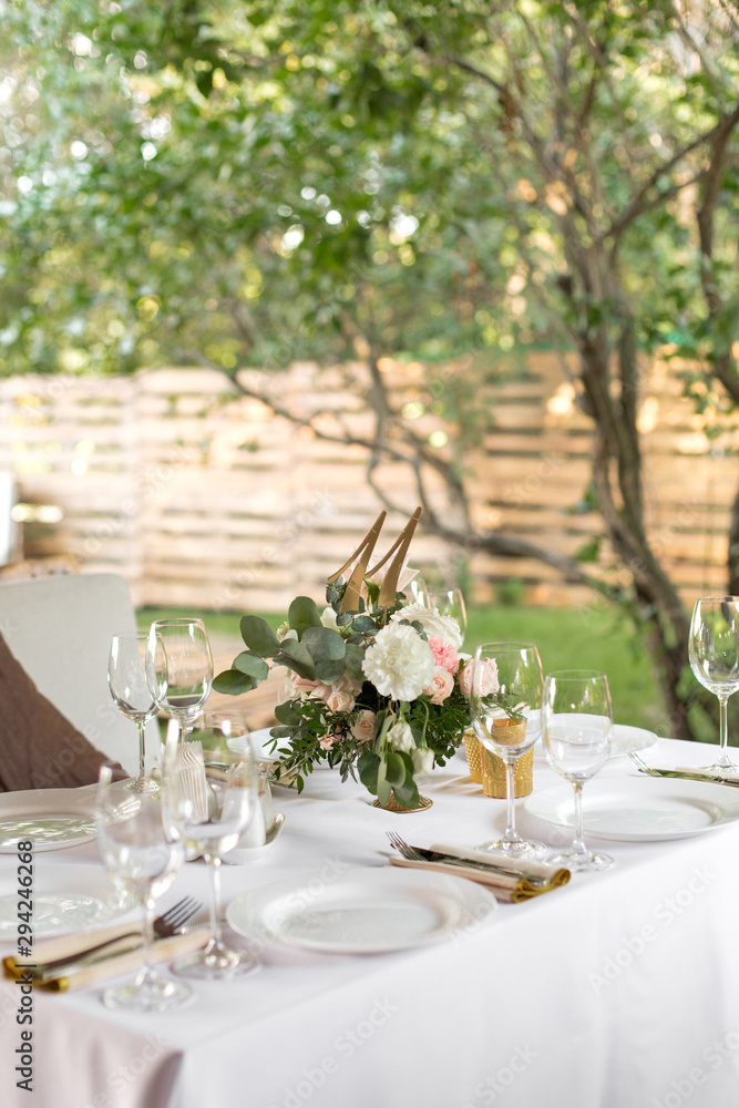 Wedding table setting decorated with fresh flowers in a brass vase. Wedding floristry. Banquet table for guests outdoors with a view of green nature. Bouquet with roses, eustoma and eucalyptus leaves Wedding table setting decorated with fresh flowers in a brass vase. Wedding floristry. Banquet table for guests outdoors with a view of green nature. Bouquet with roses, eustoma and eucalyptus leaves