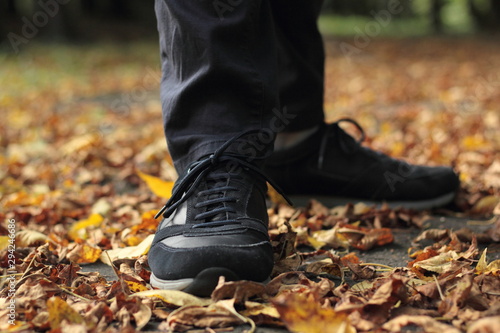 Closeup of man's legs in dark blue shoes walking in leaves on a pavement.