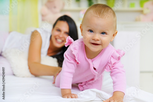 Smiling mom and baby lying in bed, baby in front , looking at camera.Shallow doff 