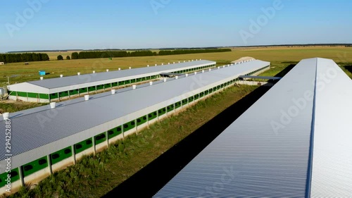 Flight over the roof of an industrial building under construction from metal profiles. Nearby are other hangars standing in a field away from the city. Taken by drone