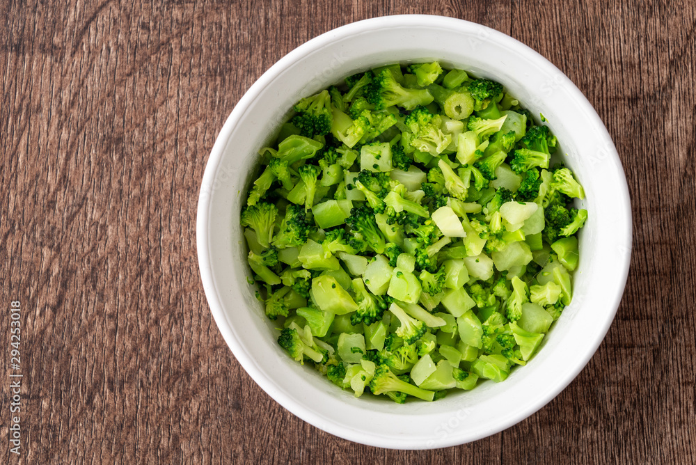 Round white bowl of chopped defrosted broccoli on a dark wood background Round white bowl of chopped defrosted broccoli on a dark wood background