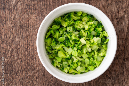 Round white bowl of chopped defrosted broccoli on a dark wood background