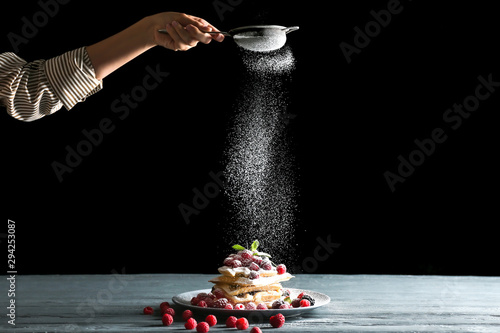 Woman sprinkling sugar powder onto Belgian wafers on table photo