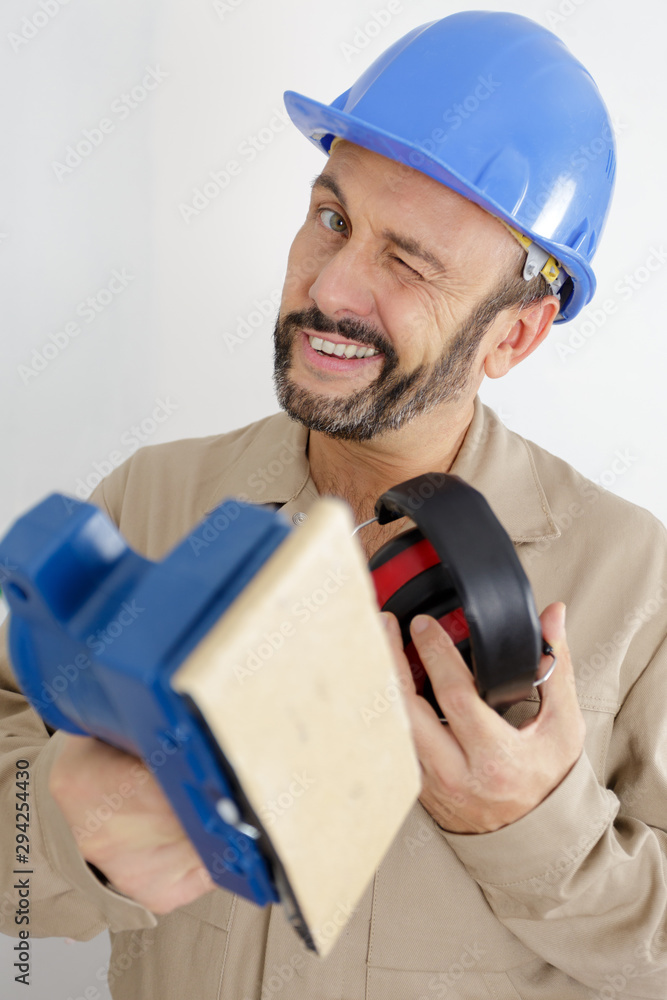 tradesman winking while holding sander and protective equipment tradesman winking while holding sander and protective equipment