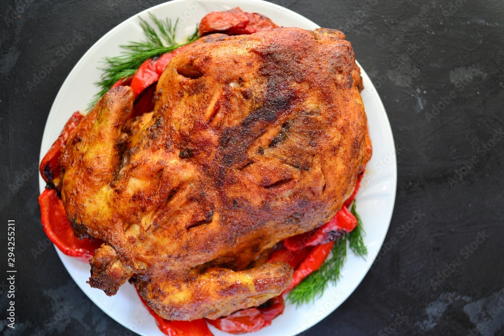 Baked whole chicken. Appetizing whole chicken in the white plate on a dark concrete table background. Festive, Christmas dish. Baked whole chicken. Appetizing whole chicken in the white plate on a dark concrete table background. Festive, Christmas dish.
