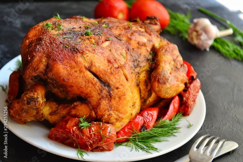 Baked whole chicken. Appetizing whole chicken in the white plate on a dark concrete table background. Festive, Christmas dish.